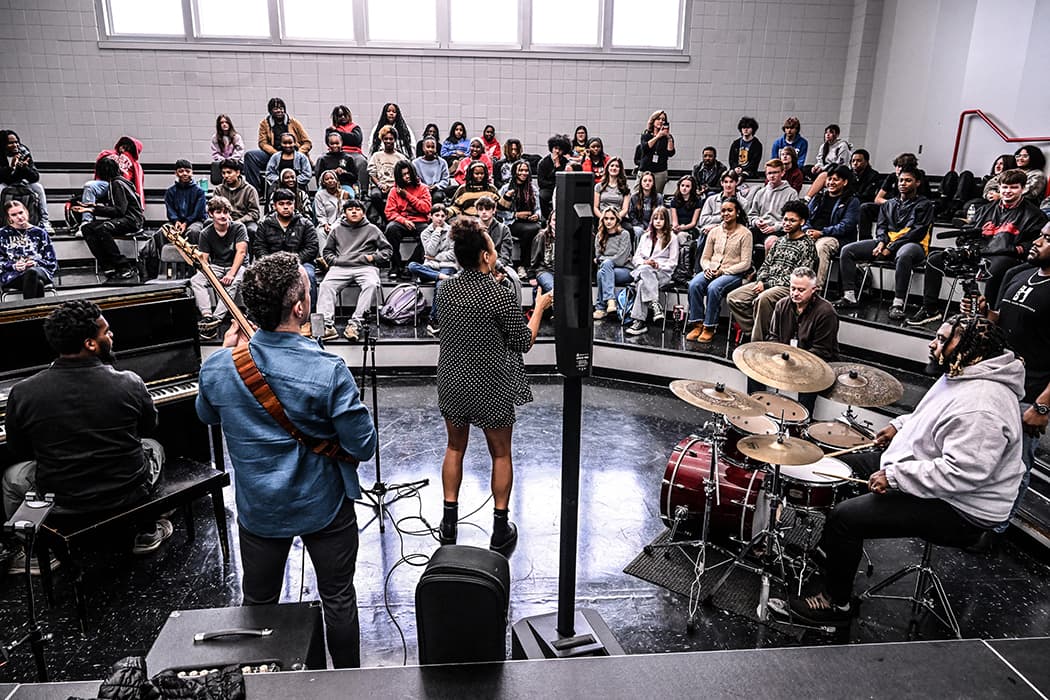 A band performing in the round for students seated on risers