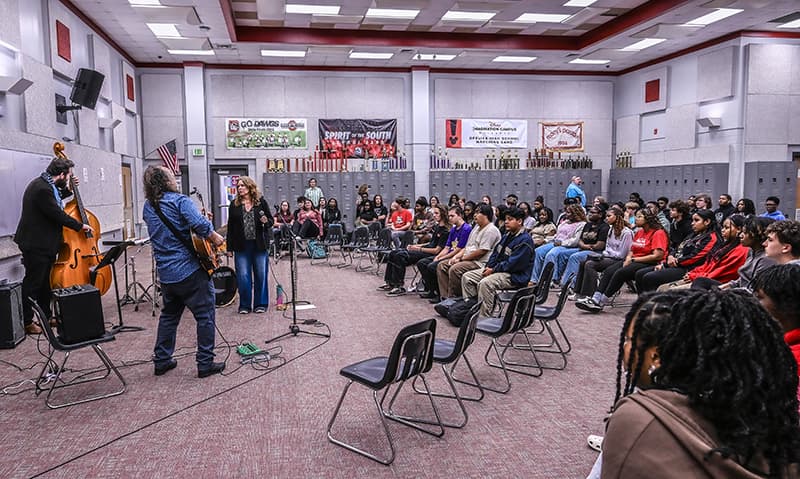 A jazz trio performing for students seated in a school band room