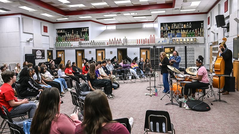 A jazz band performing for students seated in a school trophy room